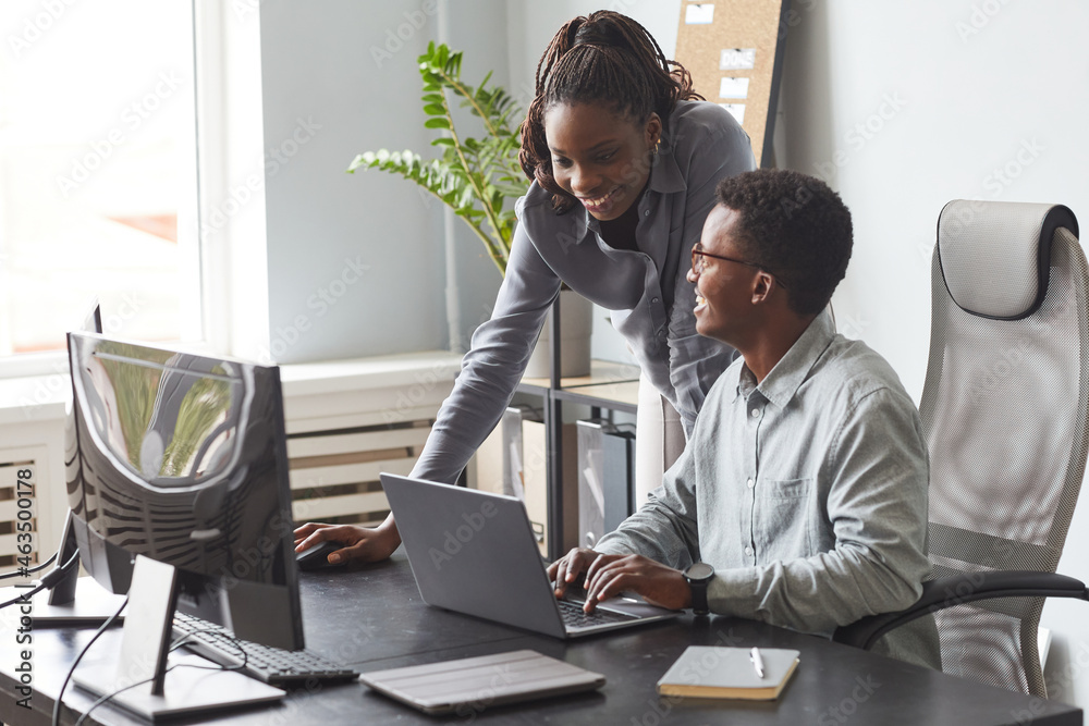 Wall mural portrait of two young people looking at computer screen and smiling while enjoying work in software 