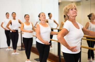 Fototapeta na wymiar Elderly woman doing ballet steps at ballet barre in the dance studio