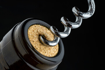 CLOSE UP OF CORKSCREW OPENING A BOTTLE OF WINE. BLACK BACKGROUND.
