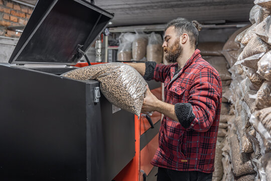 The man loads the pellets in the solid fuel boiler, working with biofuels.