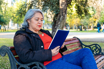 Mature woman with gray hair reading a book at park