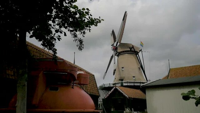 Old Dutch windmill spinning in the wind. On the back of the mill we see a rainbow flag. The windmill is part of a museum. Filmed outside museum.