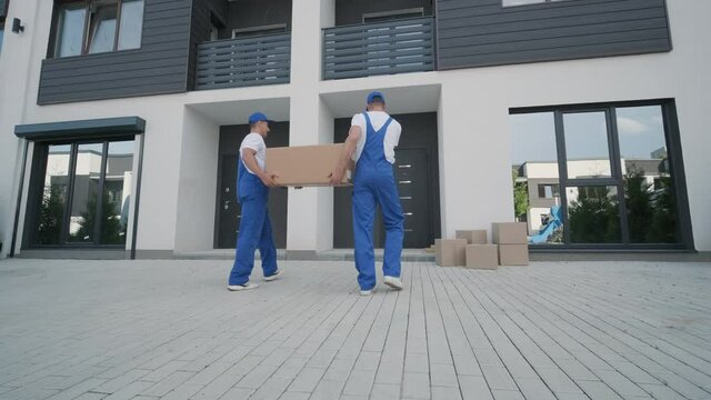 Two young workers of removal company unload boxes and furniture from minibus into customer's home