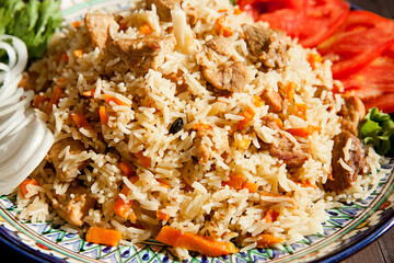 Pilaf with meat on a plate on a wooden table with herbs and tomatoes. Ramadan concept