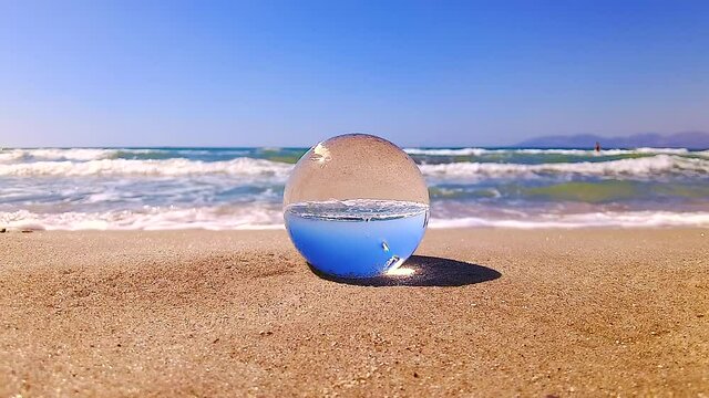 A father walks with his daughter past a glass ball lying on the beach. 