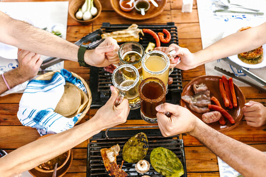 Group of Young latin Friends Meeting For beer, michelada Drinks And mexican Food Making A Toast In Restaurant terrace in Mexico Latin America	