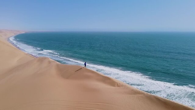 Man walks on crest of a dune next to Atlantic ocean, Namibia, aerial pan
