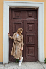 Obraz premium Young millennial woman with wild hair dressed in an autumn coat posing near the door of an old building.