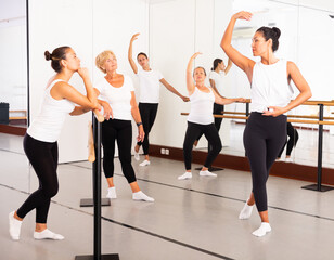 Fototapeta premium Asian woman demonstraiting ballet moves in front of women of different ages during group ballet training.