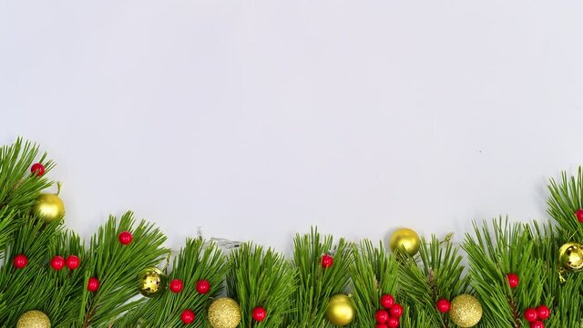Blinking lights on Christmas garland with gold ornaments and holly berries on bottom of white theme. Stop motion