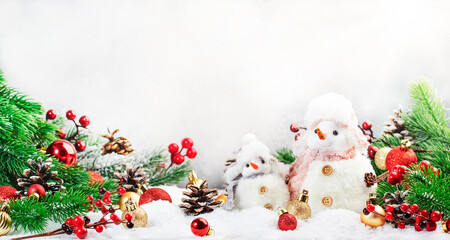 Christmas and new year snow concept with two cute snowmen in hats and scarves in snowdrift with fir branches and xmas decor on gray background