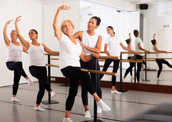 Women of different ages standing in row and training ballet moves. Trainer correcting them.