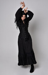 Full length portrait of dark haired woman wearing  black victorian witch costume with corset, ...