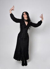 Full length portrait of dark haired woman wearing  black victorian witch costume with corset, ...