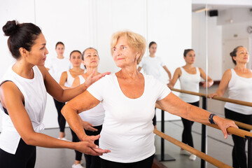 Various aged women exercising ballet dance moves. Woman trainer correcting her students.