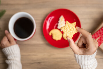 Merry Christmas with woman hand holding coffee cup and homemade cookie on table. Xmas eve, party, holiday and happy New Year concept