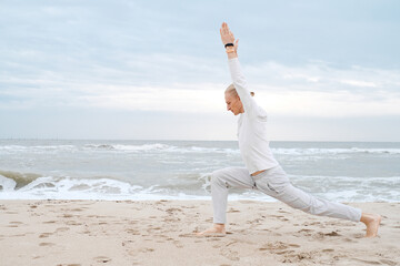 Man doing yoga on the beach in autumn over waves in the sea. Creamy, light sand and sky, Asanas and...