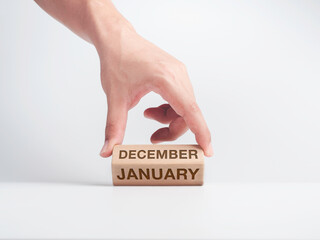 Changing to the first month of the year. The hand is flipping wooden cube blocks for change words, months from December to January on the desk on white background, clean, modern, and minimal style.