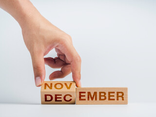 Changing to the last month of the year. The hand is flipping wooden cube blocks for change words, months from November to December on the desk on white background, clean, modern, and minimal style.