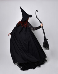 Full length portrait of dark haired woman wearing  black victorian witch costume with  cloak and...