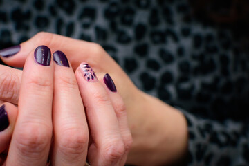 Detalle de uñas pintadas con motivo floral en violeta y rosa con fondo desenfocado