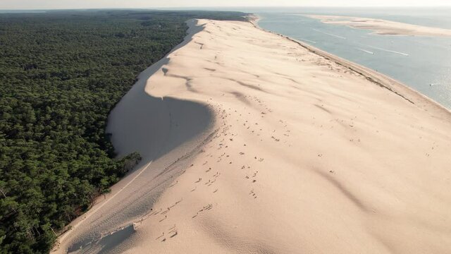 People over dune of Pilat at sunset, Arcachon basin in France. Aerial forward