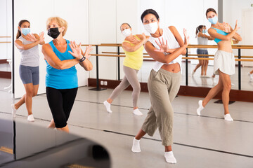 Fototapeta na wymiar Women in protective mask practicing vigorous dance movements in group dance class