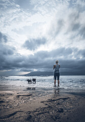 A woman playing with the dogs at the beach.