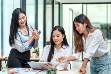 Fototapeta premium Team of young Asian businesswomen in a brainstorming meeting using a tablet to take notes graph at the office.