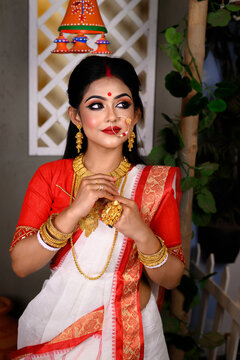 Portrait of beautiful Indian Bengali female woman in red and white traditional ethnic saree and jewellery in studio lighting indoor. Indian culture, religion and fashion