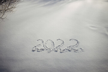 Drawing on white snow in sunlight. New Year's date, figures 2022, close-up.