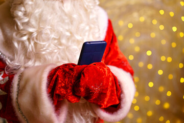 Santa claus's hand in mittens holds smartphone in his hands. Long white beard, red suit. Modern russian grandfather frost. New year's order processing