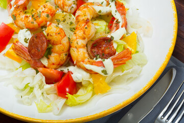 Appetizing salad with fried shrimps, chorizo sausages, fresh vegetables and lemon