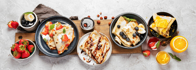 Sweet crepes assortment with berries chocolate on gray background.