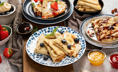 Sweet crepes assortment with berries chocolate on gray background.