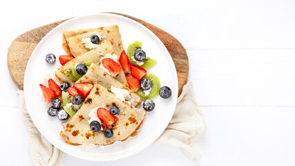 Sweet crepes with berries and cream on white wooden background.
