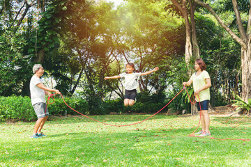 Asian family playing together and daughter jumping over the rope in the park.