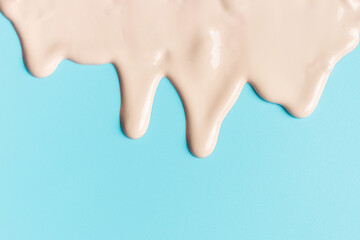 A beige foundation drips down on blue background close-up.