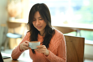 Young asian woman in sweater holding cup of tea or coffee.