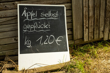 on a black board is written with white chalk: Apples picked by the farmer, kilogram 1.20€. A chalkboard stands against a brown wooden wall. 