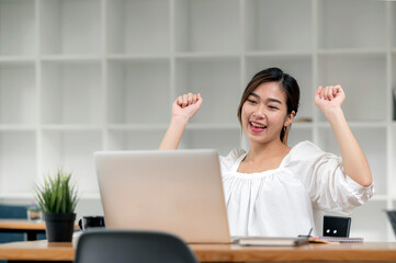 asian woman sitting at desk with laptop and feel euphoric win.