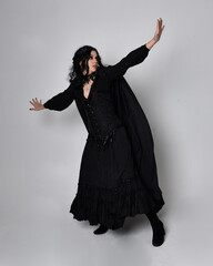 Full length portrait of dark haired woman wearing  black victorian witch costume with a flowing ...