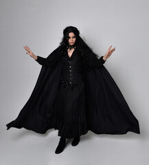 Full length portrait of dark haired woman wearing  black victorian witch costume with a flowing ...