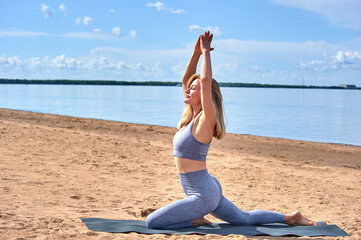 Fototapeta na wymiar A woman does yoga on a sandy beach against the background of a river