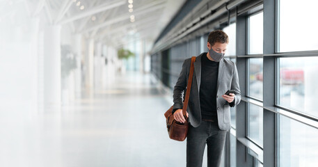 Travel business man wearing coronavirus face mask walking in airport using vaccine passport mobile...