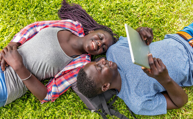 Afro american couple relaxing happy on the grass looking at tablet screen, downward view
