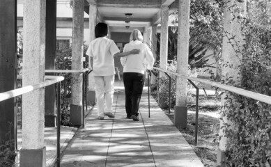 Asian doctor helping elderly retired woman with walker stick in the hospital yard. Rehabilitation concept