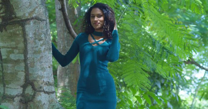 Slim curly hair girl stands next to a large tree trunk on a tropical island