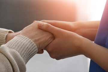 Nurse holding hands of elderly woman at home, closeup