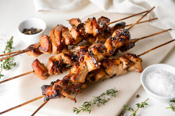 Board with grilled chicken skewers on light background